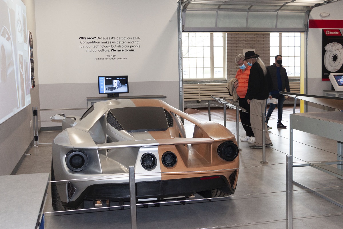Two people look at a low race car in a museum exhibit space that looks like a garage
